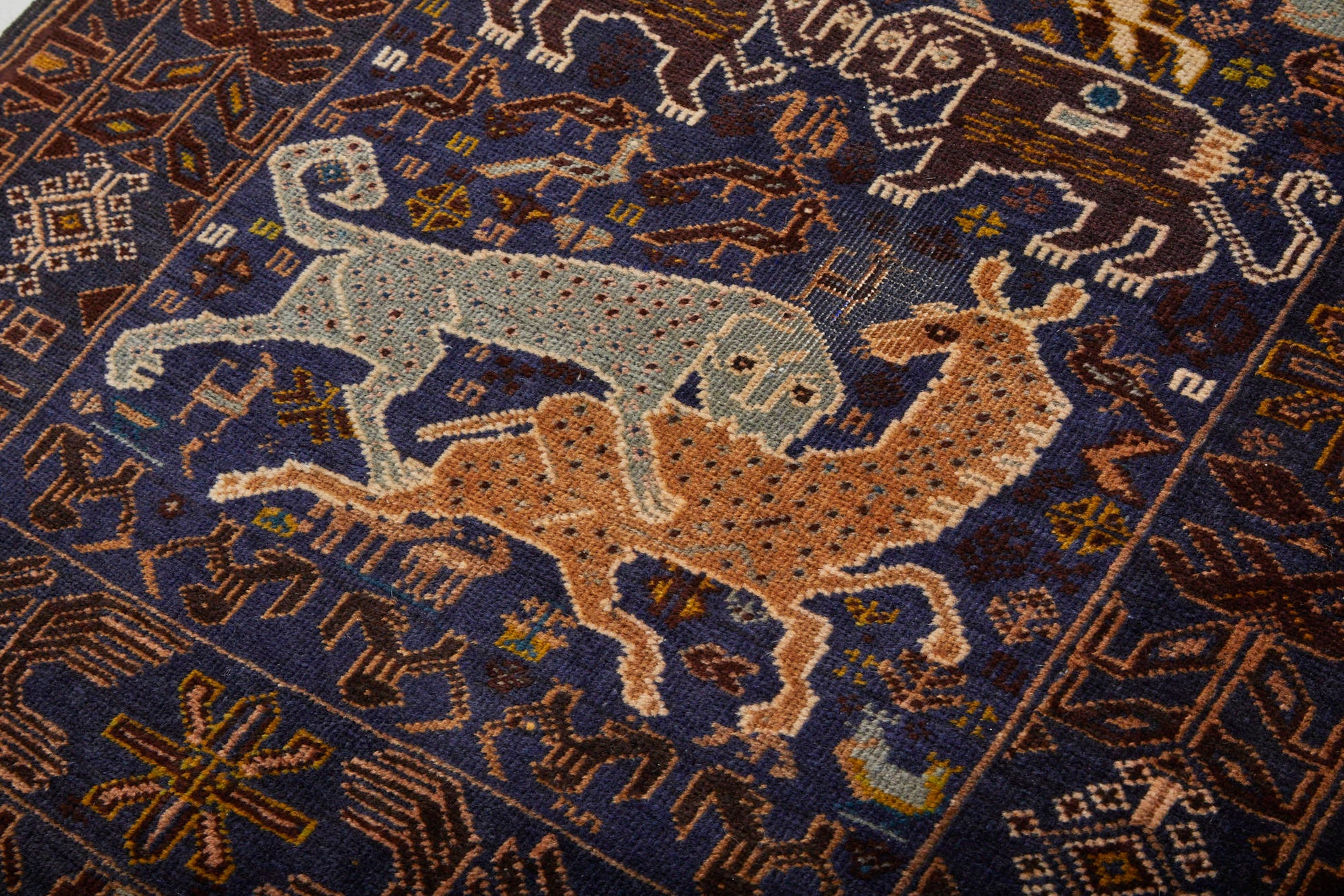 Detail of handwoven Afghan Shikargah pictorial rug depicting leopard or tiger attacking a deer on dark blue background, surrounded by symbols -  Available from King Kennedy Rugs Los Angeles