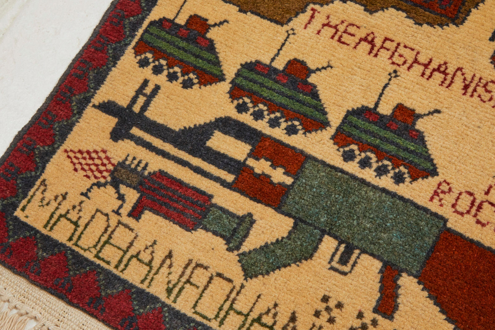 Hand woven Afghan war rug with map images, tanks, weapons and the words "Pakistan," "2015," "Made in Afghanistan" with cream background and red, brown and blue images - Available from King Kennedy Rugs Los Angeles