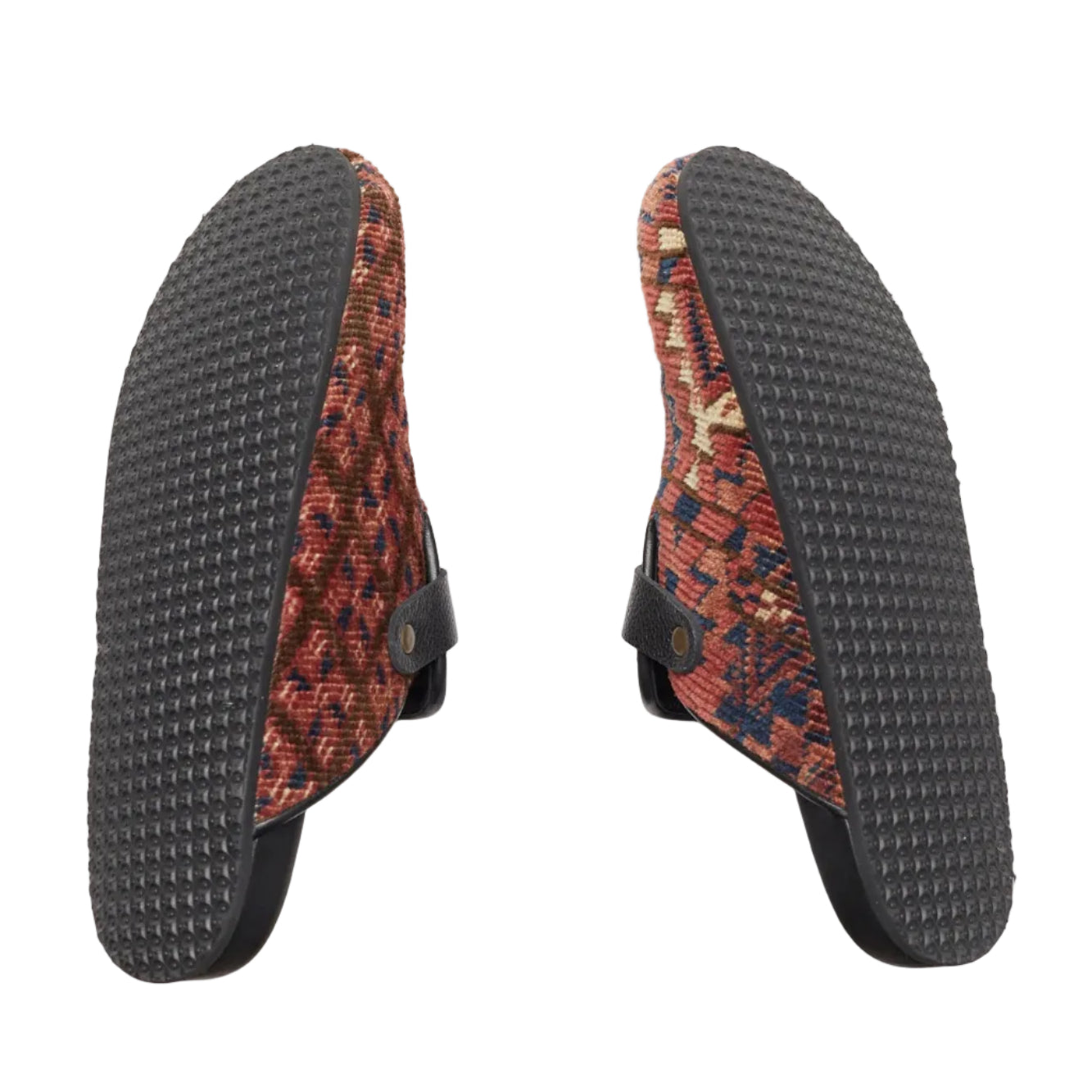 Rubber sole view of carpet mules. King Kennedy Rug Mules are one-of-a-kind and made of 100 year old antique Persian rug fragments with soft lambskin footbed and comfortable rubber sole. This pair is made of an antique Persian rug with a beautifully faded red pink base and blue, cream and tan diamond shaped designs throughout.