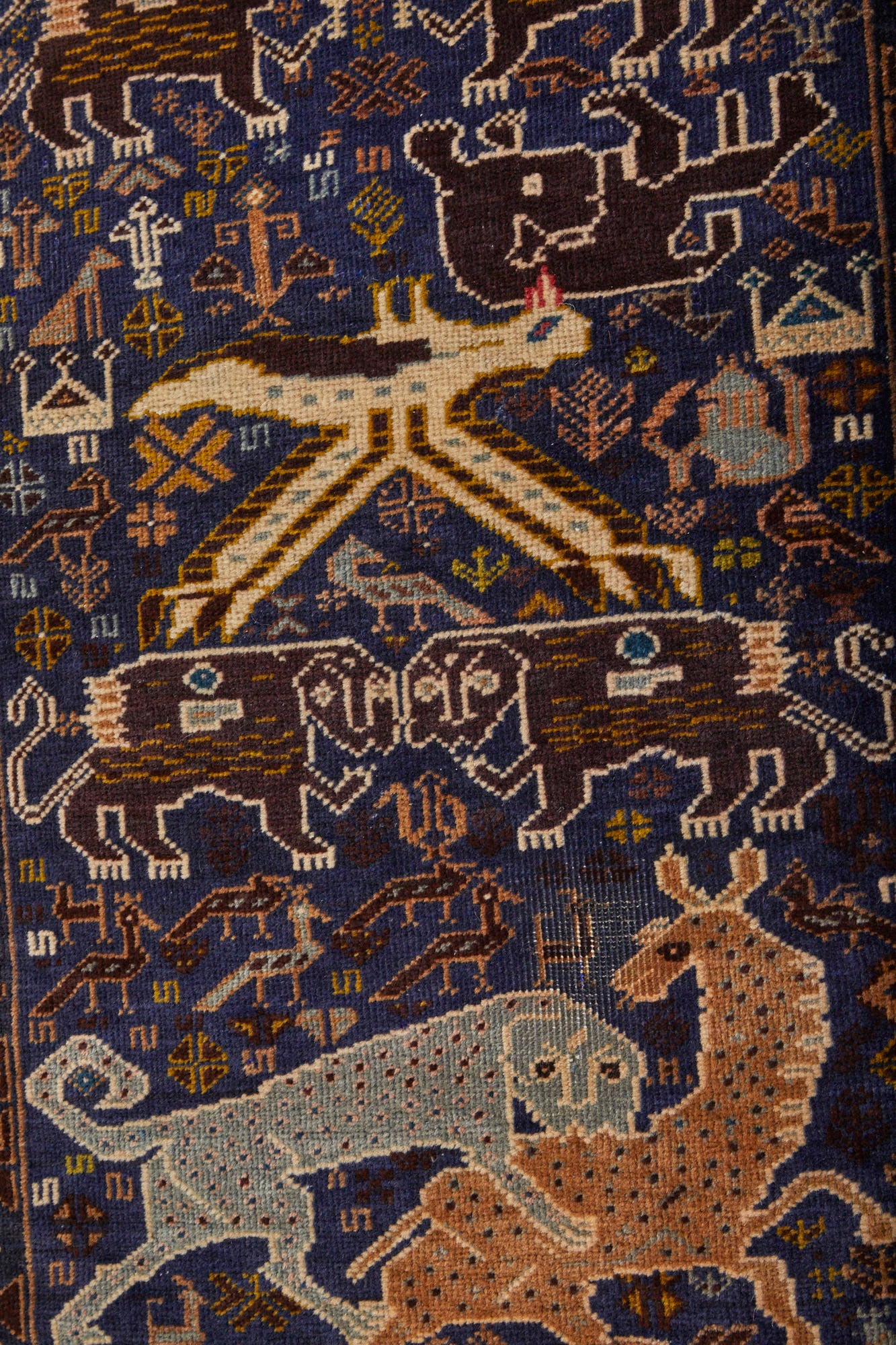 Close-up of handwoven Afghan Shikargah pictorial rug depicting leopard or tiger attacking a deer on dark blue background, surrounded by symbols -  Available from King Kennedy Rugs Los Angeles