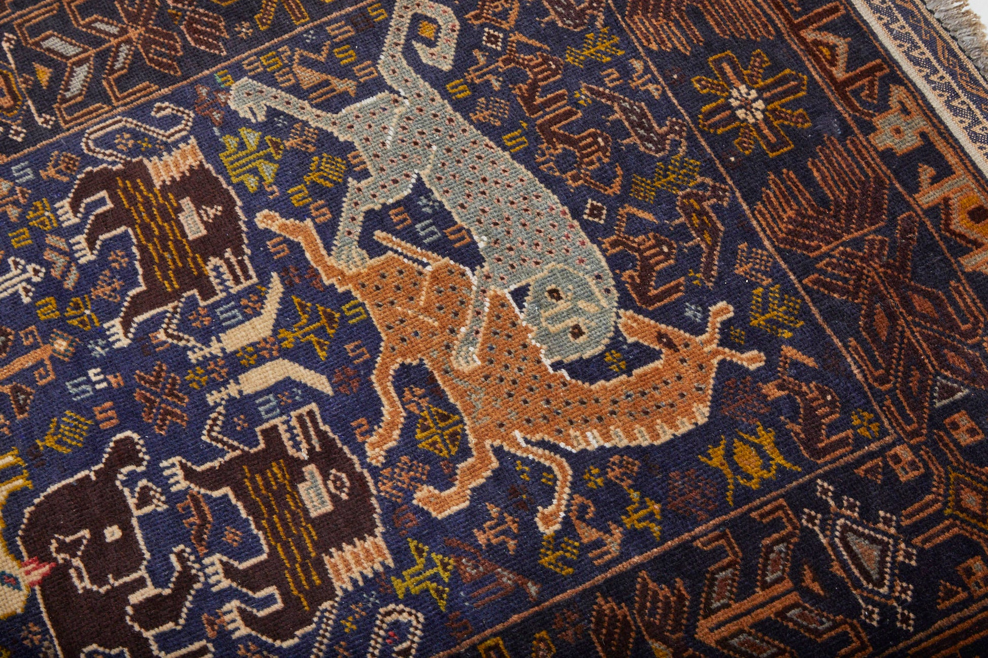 Detail of hand woven Afghan Shikargah pictorial rug depicting leopard or tiger attacking a deer on dark blue background, surrounded by symbols -  Available from King Kennedy Rugs Los Angeles