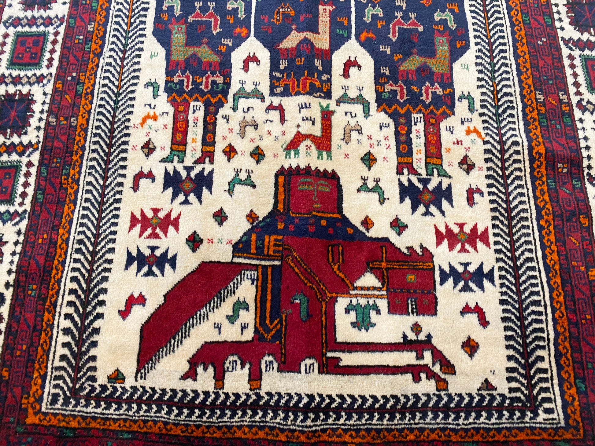 Detail of Afghan pictorial rug with cream base and three figures in blue cloaks across the middle, figures with crowns on horses at the top and bottom of rug woven in deep blue and reds