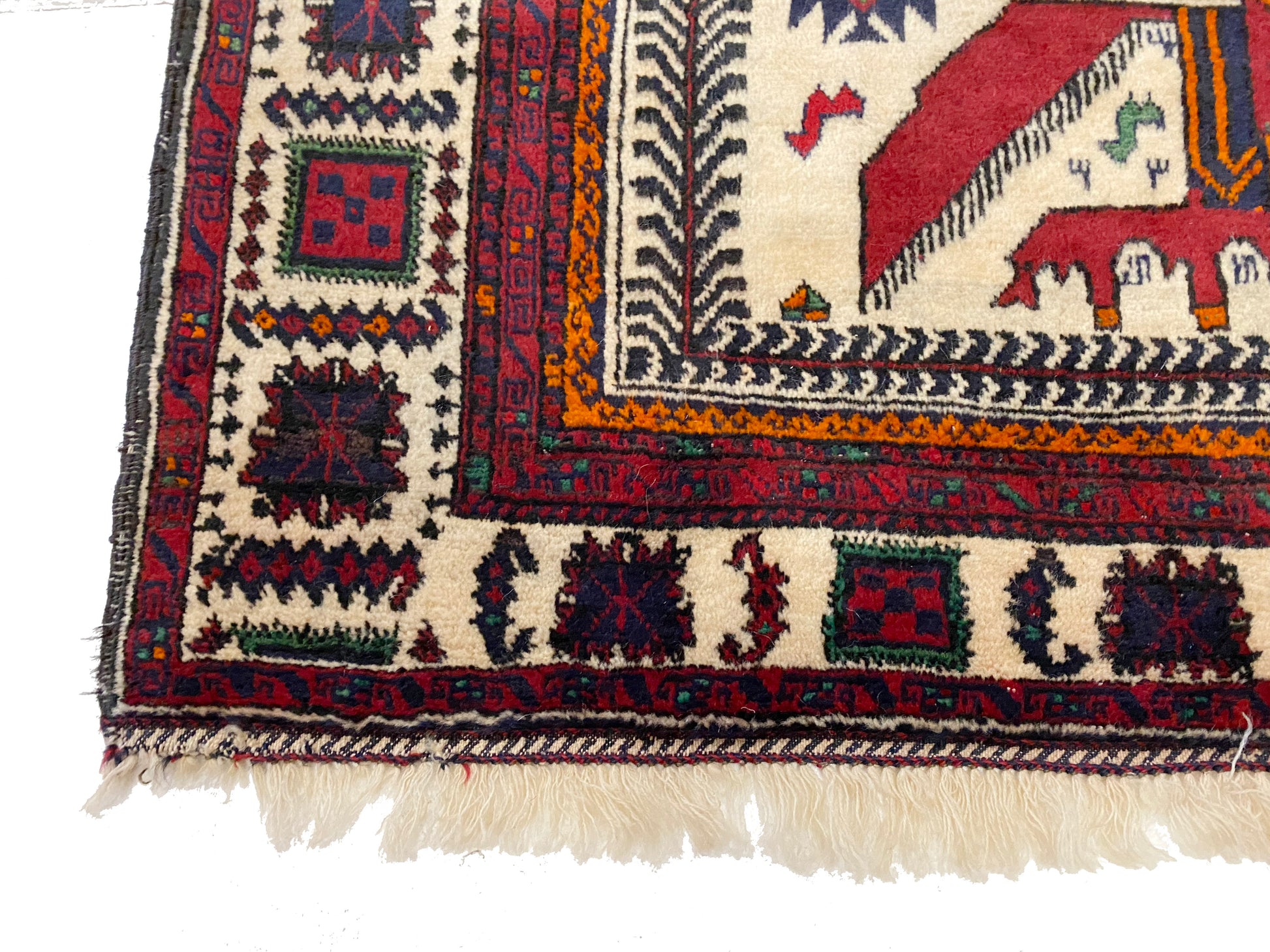 Detail of lower corner of Afghan pictorial rug with cream base and three figures in blue cloaks across the middle, figures with crowns on horses at the top and bottom of rug woven in deep blue and reds