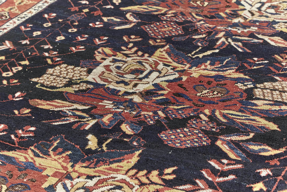 Rose detail on Antique hand woven Caucasian rug, depicting three clusters of roses. Beautiful dark blue base with red and cream roses. Red border with cream, gold and brown shapes. Perfect for a bedroom or study. Available from King Kennedy Rugs Los Angeles