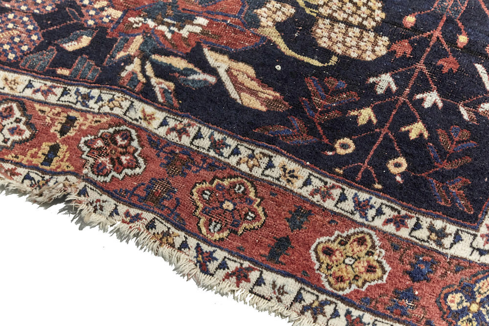 Antique hand woven Caucasian rug, depicting three clusters of roses. Beautiful dark blue base with red and cream roses. Red border with cream, gold and brown shapes. Perfect for a bedroom or study. Available from King Kennedy Rugs Los Angeles