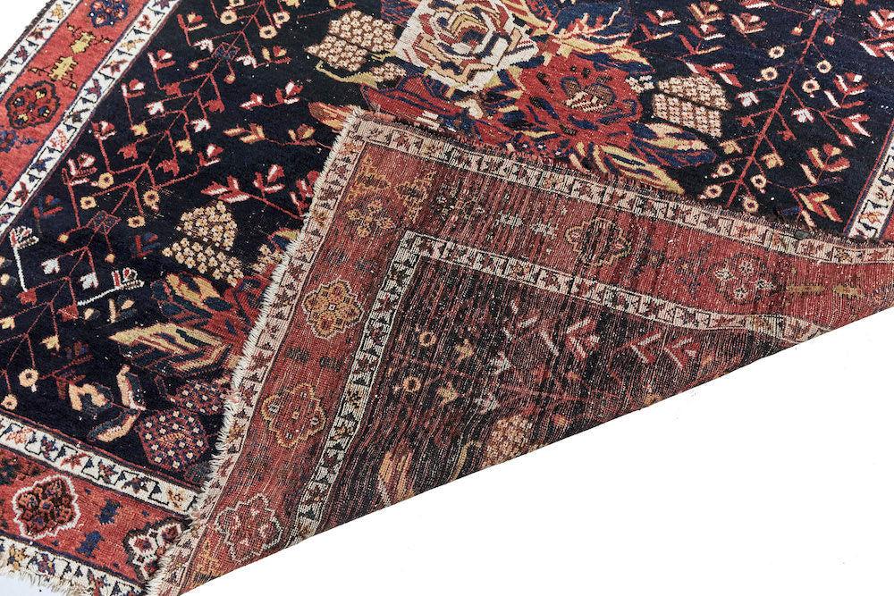 Front and back of Antique hand woven Caucasian rug, depicting three clusters of roses. Beautiful dark blue base with red and cream roses. Red border with cream, gold and brown shapes. Perfect for a bedroom or study. Available from King Kennedy Rugs Los Angeles
