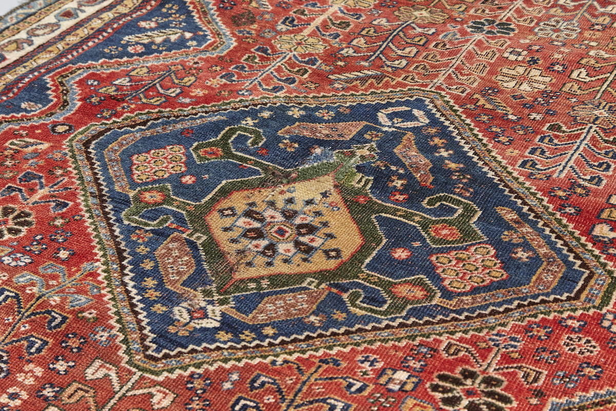 Center detail of Kashkai antique Persian rug with red base, cream border and deep blue details. Plants and flowers woven throughout. Perfect for a bedroom or study.Available from King Kennedy Rugs Los Angeles
