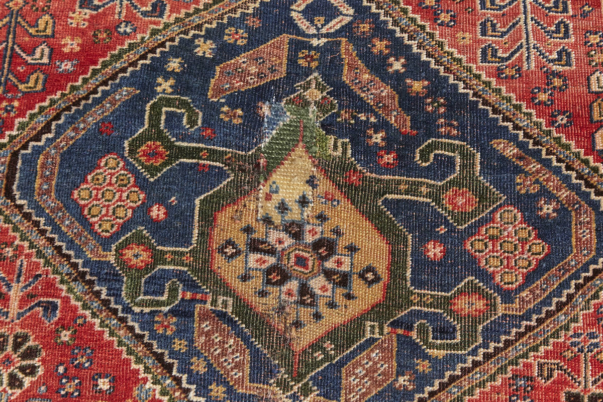 Repair detail of Kashkai antique Persian rug with red base, cream border and deep blue details. Plants and flowers woven throughout. Perfect for a bedroom or study.Available from King Kennedy Rugs Los Angeles