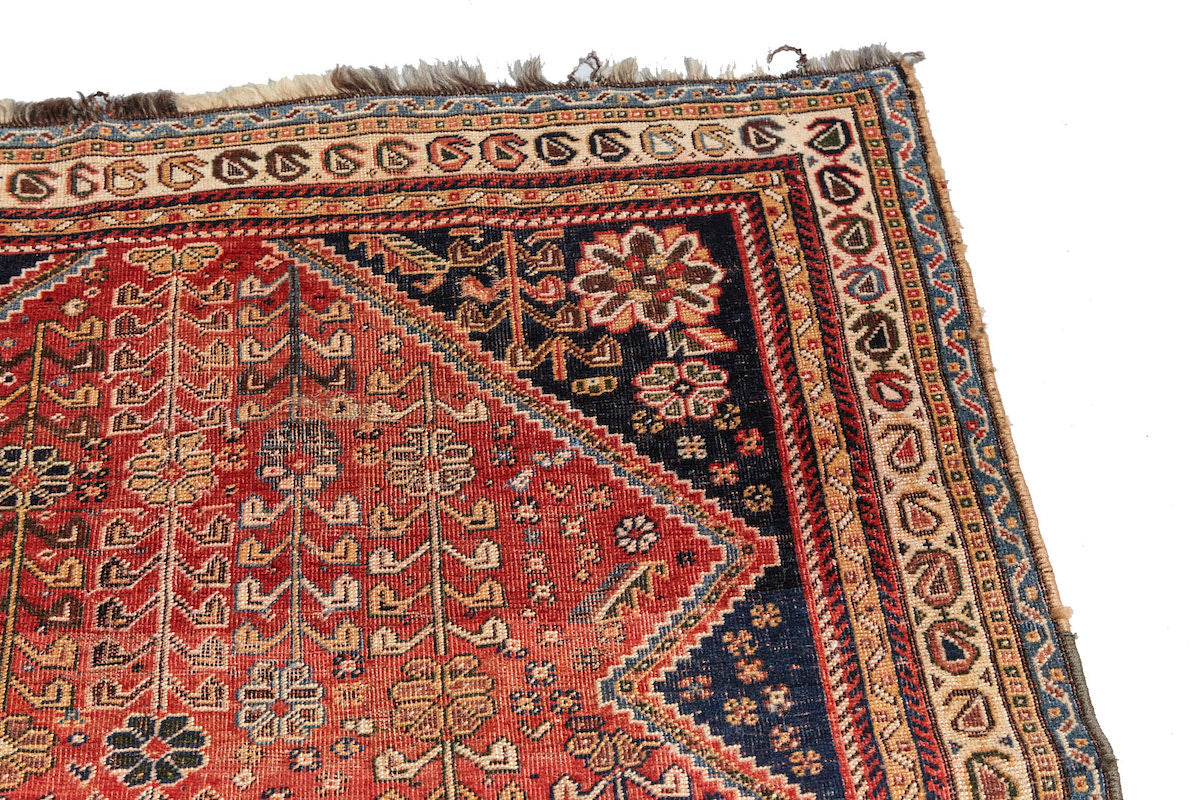 Kashkai antique Persian rug with red base, cream border and deep blue details. Plants and flowers woven throughout. Perfect for a bedroom or study.Available from King Kennedy Rugs Los Angeles