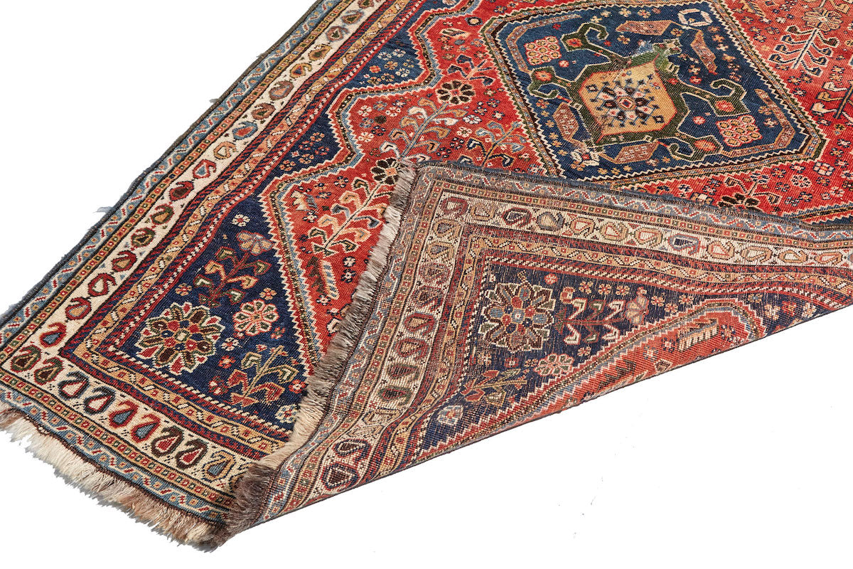 Front and back of Kashkai antique Persian rug with red base, cream border and deep blue details. Plants and flowers woven throughout. Perfect for a bedroom or study.Available from King Kennedy Rugs Los Angeles