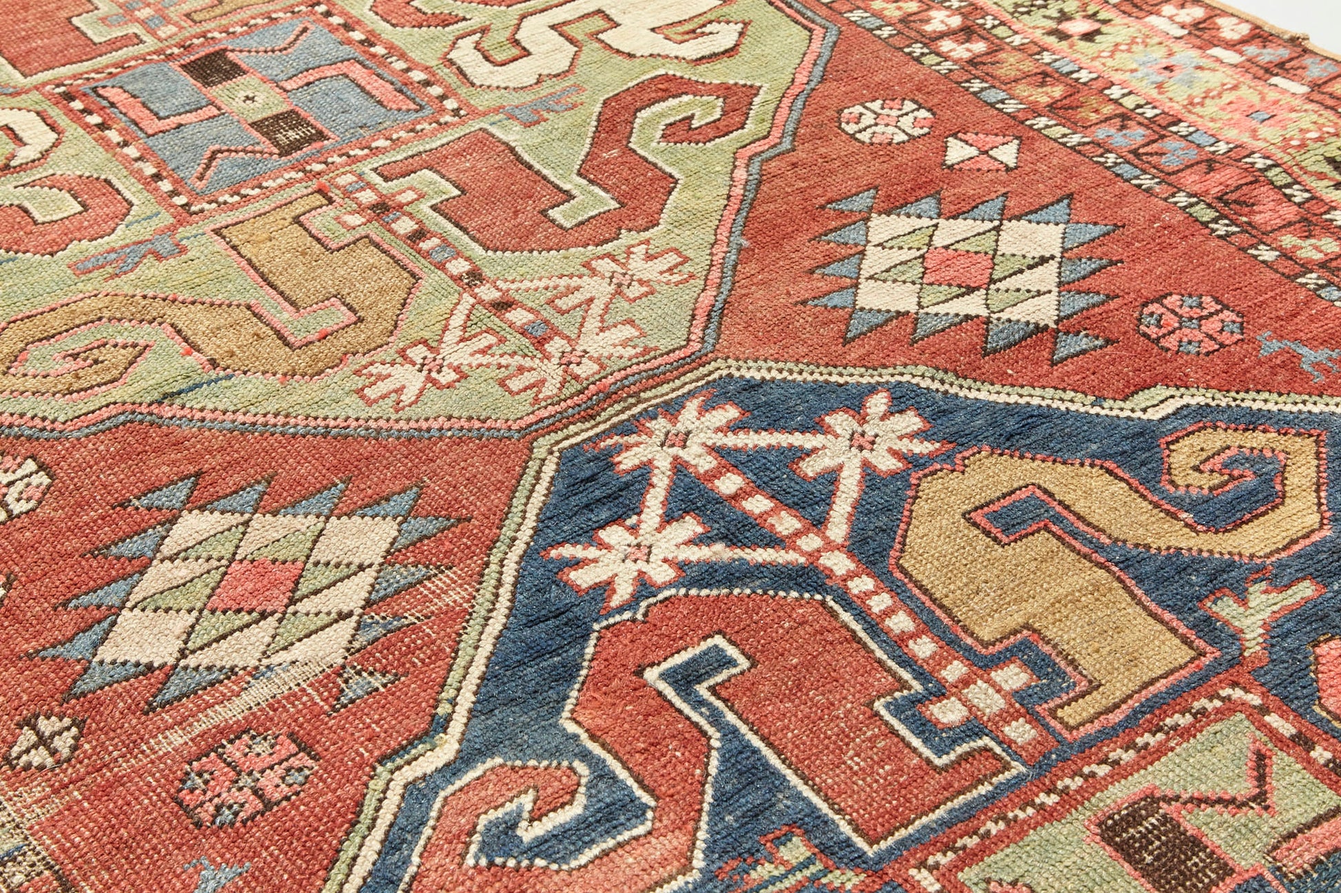 Detail of Kazak Cloudband antique Persian rug with rich pink base and two large medallion designs in the center, one pale green, one blue with pink, red, gold, cream and blue designs intricately hand woven throughout. A beautiful piece for a bedroom, hallway, dining room or study - Available from King Kennedy Rugs Los Angeles