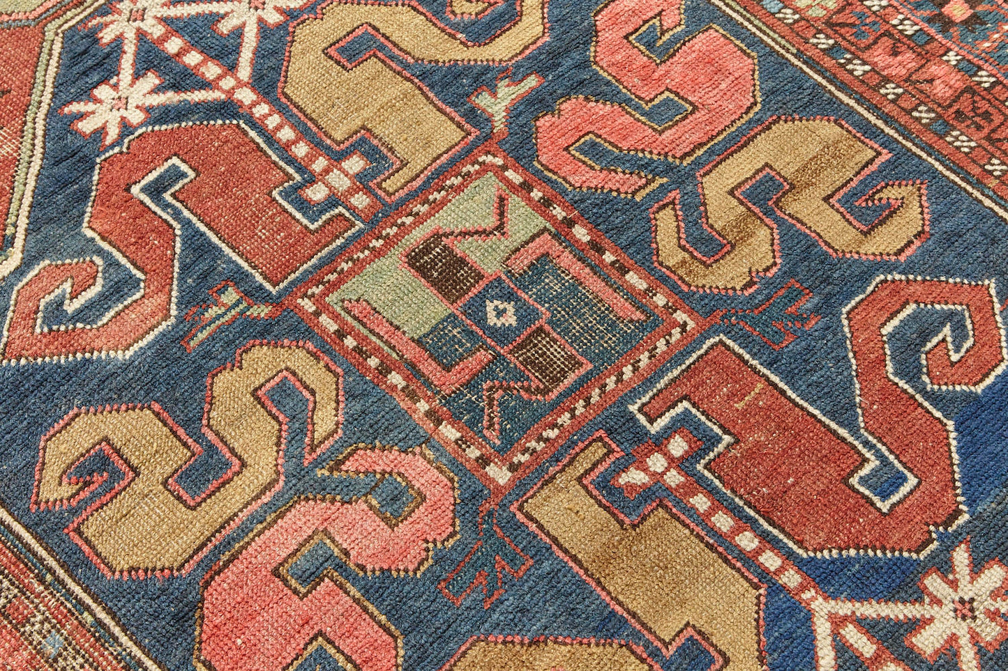 Detail of Kazak Cloudband antique Persian rug with rich pink base and two large medallion designs in the center, one pale green, one blue with pink, red, gold, cream and blue designs intricately hand woven throughout. A beautiful piece for a bedroom, hallway, dining room or study - Available from King Kennedy Rugs Los Angeles