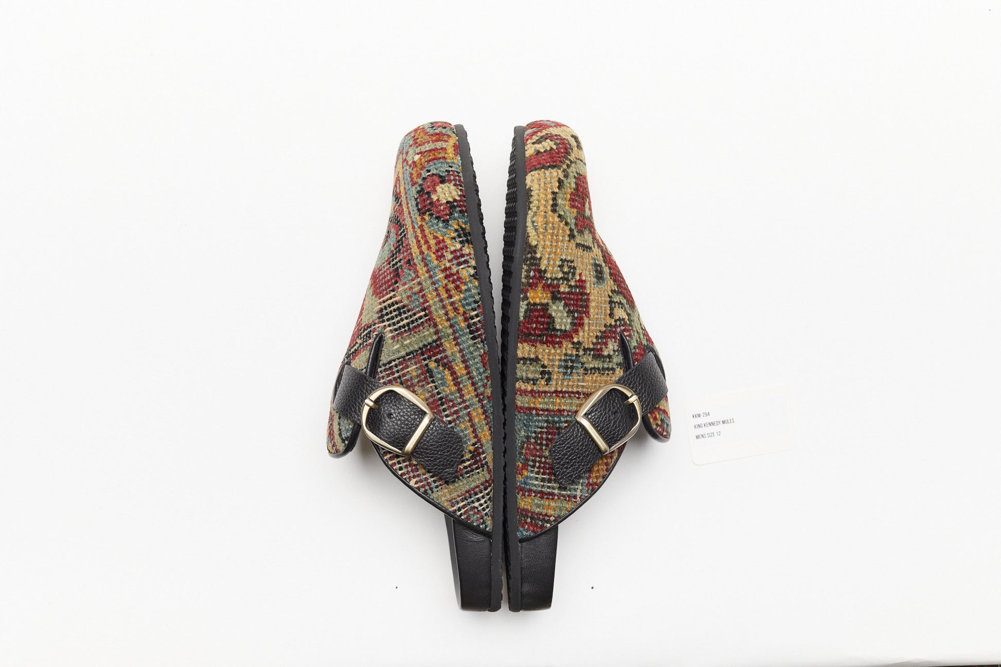 Buckle side view of rug mules.  King Kennedy Rug Mules are one-of-a-kind and made of 100 year old antique Persian rug fragments with soft lambskin footbed and comfortable rubber sole. This pair is made of an antique Persian rug with gold, red and faded blue patterns. 