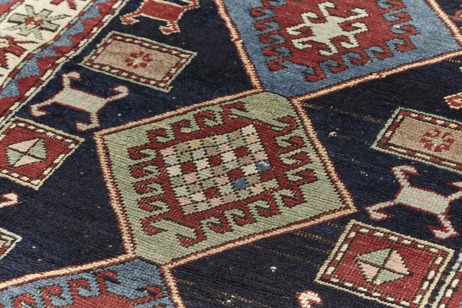 Detail of Antique hand woven Kazak Persian rug with dark blue base, blue and pale green diamonds across center with a cream and red border, featuring red, pale green and blue star-like shapes. Perfect for bedroom, living room dining room or kitchen. Available from King Kennedy Rugs Los Angeles.