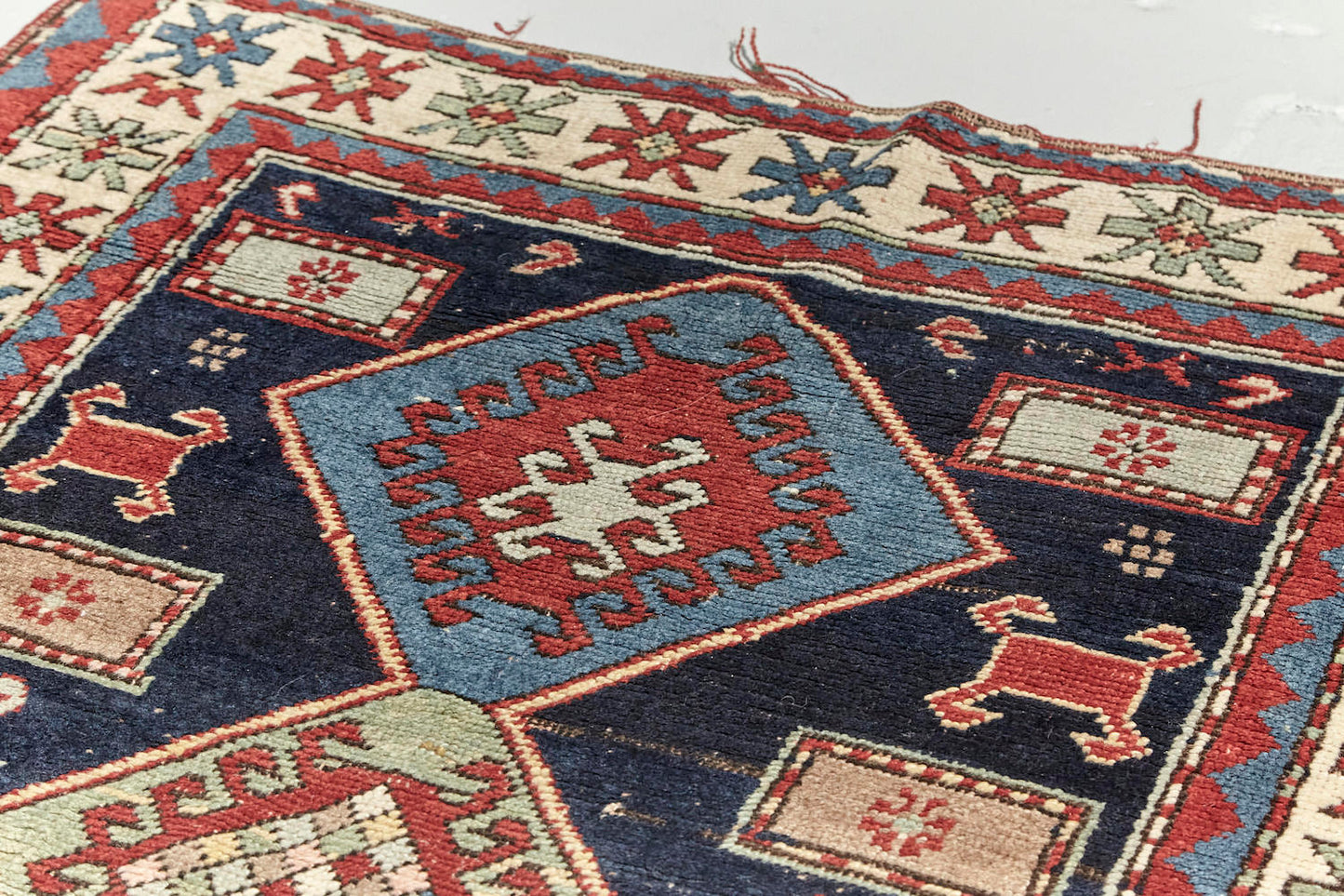Antique hand woven Kazak Persian rug with dark blue base, blue and pale green diamonds across center with a cream and red border, featuring red, pale green and blue star-like shapes. Perfect for bedroom, living room dining room or kitchen. Available from King Kennedy Rugs Los Angeles.