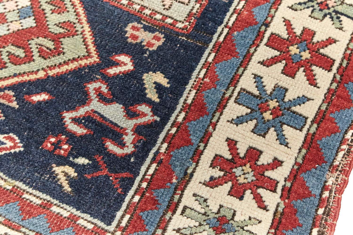 Antique hand woven Kazak Persian rug with dark blue base, blue and pale green diamonds across center with a cream and red border, featuring red, pale green and blue star-like shapes. Perfect for bedroom, living room dining room or kitchen. Available from King Kennedy Rugs Los Angeles.