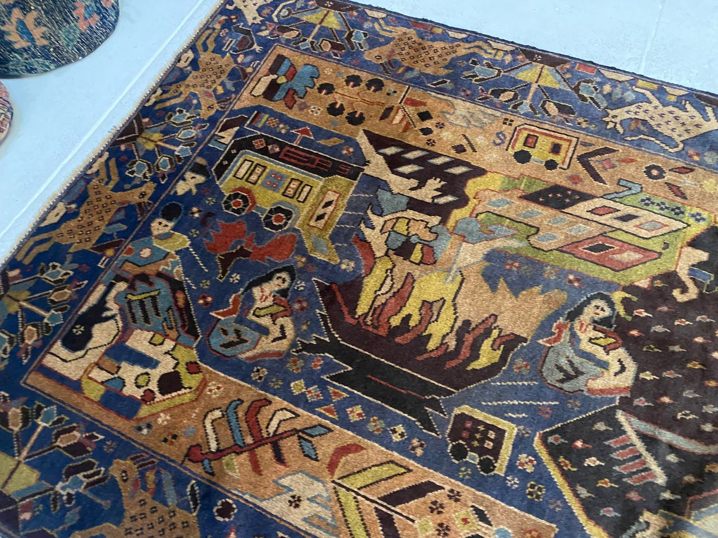 Detailed hand woven Afghan Pictorial Rug depicting figures around a fire near a caravan, along with deep blue hues with beige, black and pale green details of plants and animals. Perfect for a bedroom, living room, studio or study.Available from King Kennedy Rugs Los Angeles
