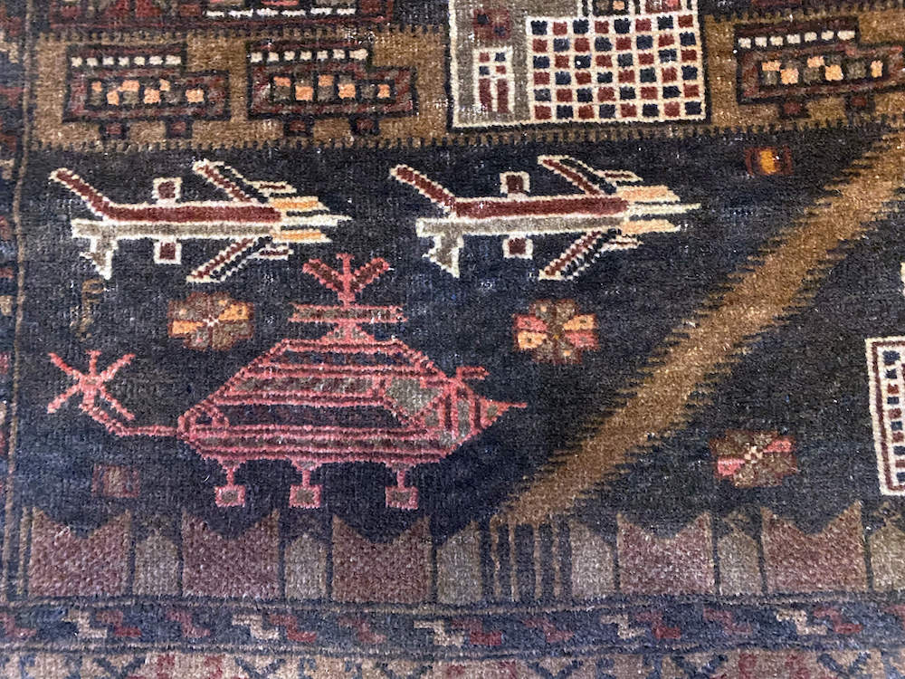 Hand woven Afghan war rug with buildings, planes and helicopters. Hand woven in deep brown with cream, red and orange details. Perfect for a study, kitchen or bedroom. Available from King Kennedy Rugs Los Angeles