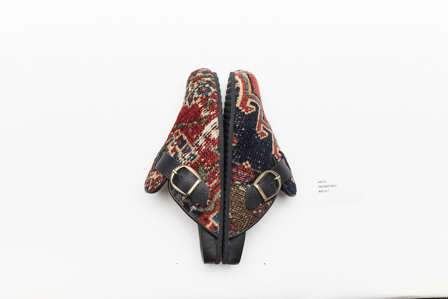 Buckle side view of these one-of-a-kind mules made of 100 year old antique Persian rug fragments with soft lambskin footbed and rubber sole. Similar in shape to the Birkenstock Boston clog. These men's size 7 are made of an antique red, blue and white rug with zig zag patterns.
